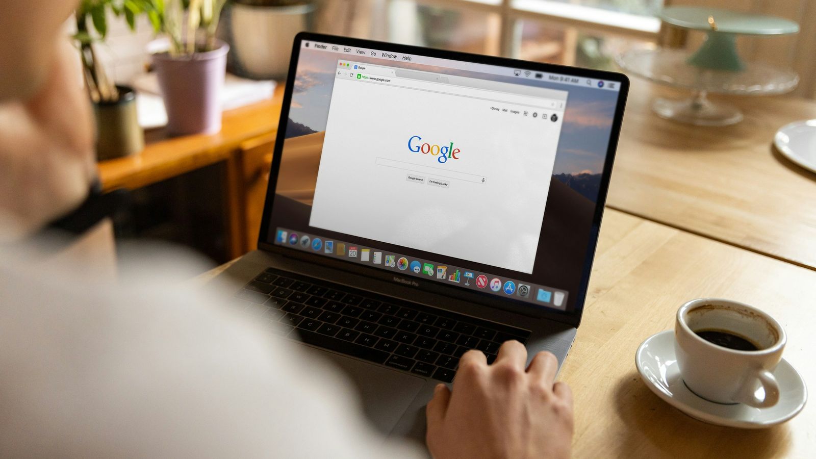 Person at a laptop open on the Google search page, with a coffee beside them.